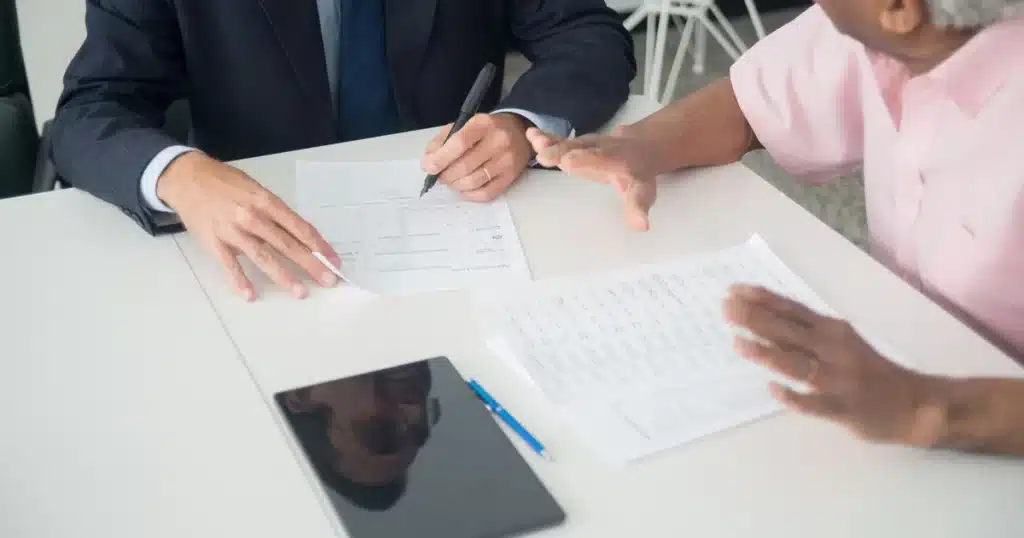 Abus financier sur personne âgée : identifier, prouver et agir 3 Personne âgée examinant attentivement des documents financiers à un bureau en bois, à la lumière naturelle.