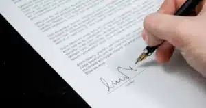 Mains écrivant une lettre administrative sur un bureau avec dossiers, lumière naturelle douce.