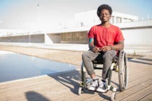 Jeune homme en fauteuil roulant, souriant, sur une promenade au bord de l'eau